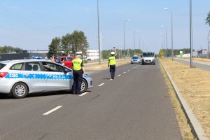 Na zdjęciu radiowóz i policjantki, jedna z policjantek zatrzymuje pojazd do kontroli drogowej.